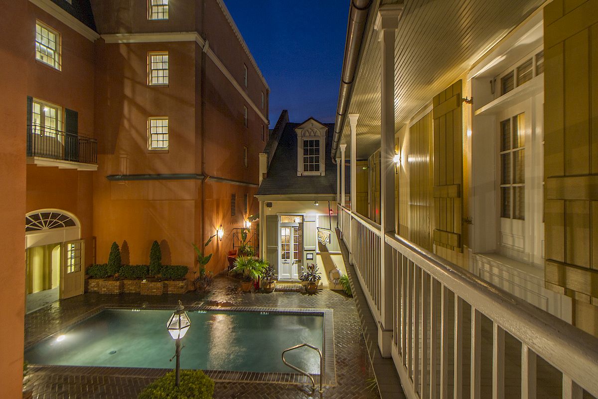 A nighttime courtyard view with a lit swimming pool, surrounded by buildings featuring windows and balconies, and exterior lighting.